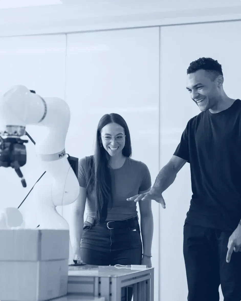 deux ingénieurs sont dans un bureau et sourient en regardant un prototype de bras robotisé