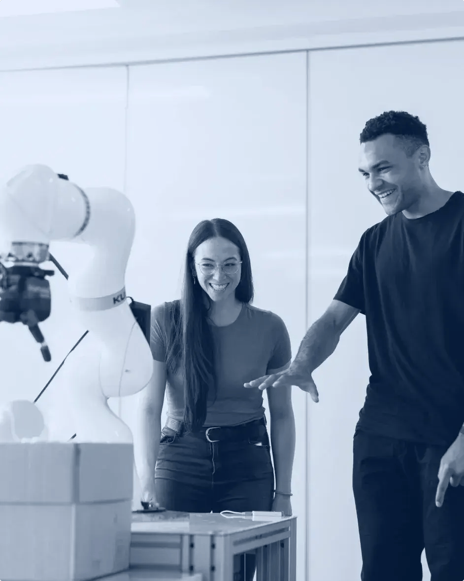 un homme et une femme regardent un bras robotisé en souriant