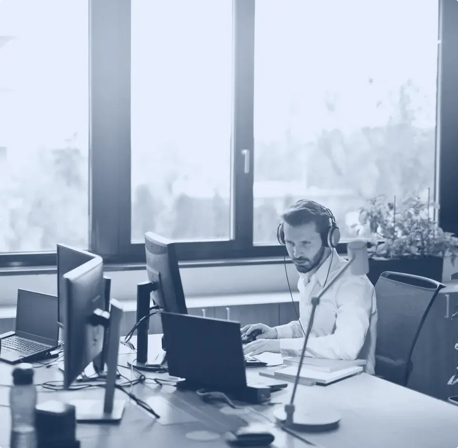 un homme assis devant son bureau, qui porte un casque et travaille